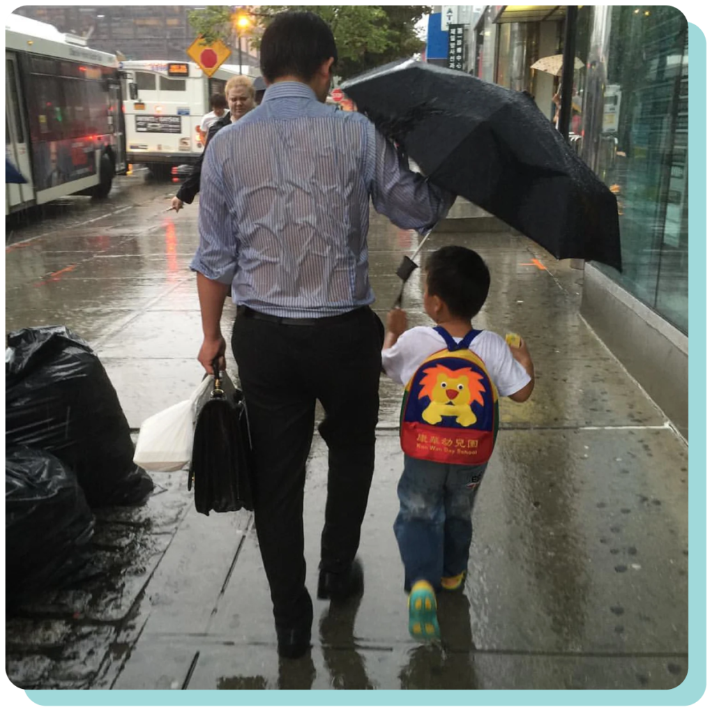 Asian dad holding umbrella for kid